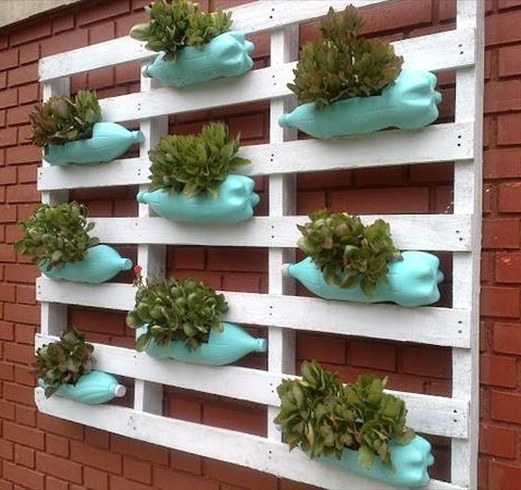 Un exemple inspirant de mini-potager recyclé utilisant des bouteilles en plastique et des palettes en bois pour cultiver des herbes aromatiques et des petites laitues sur un balcon